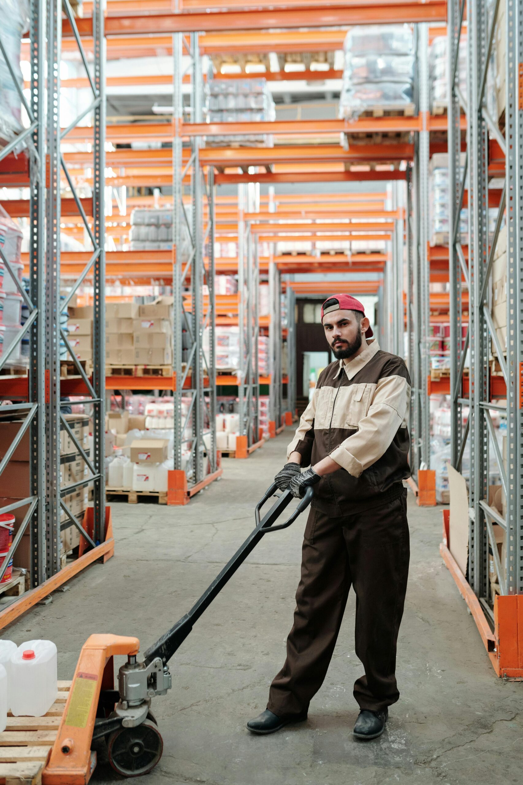 Man in uniform using a pallet jack in a well-organized warehouse storeroom.