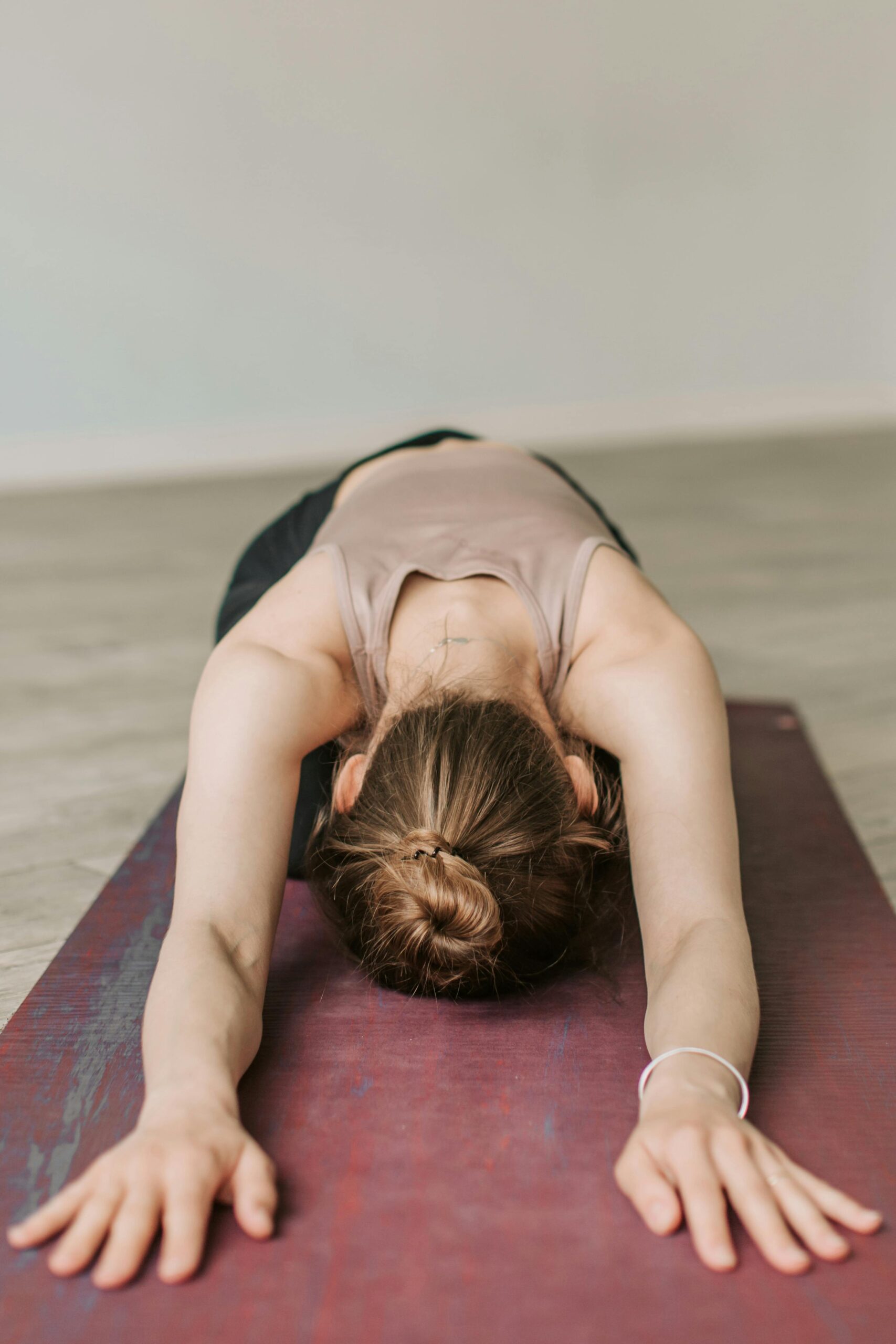 A woman in a child's pose during a yoga session on a red mat indoors, promoting relaxation and wellness.